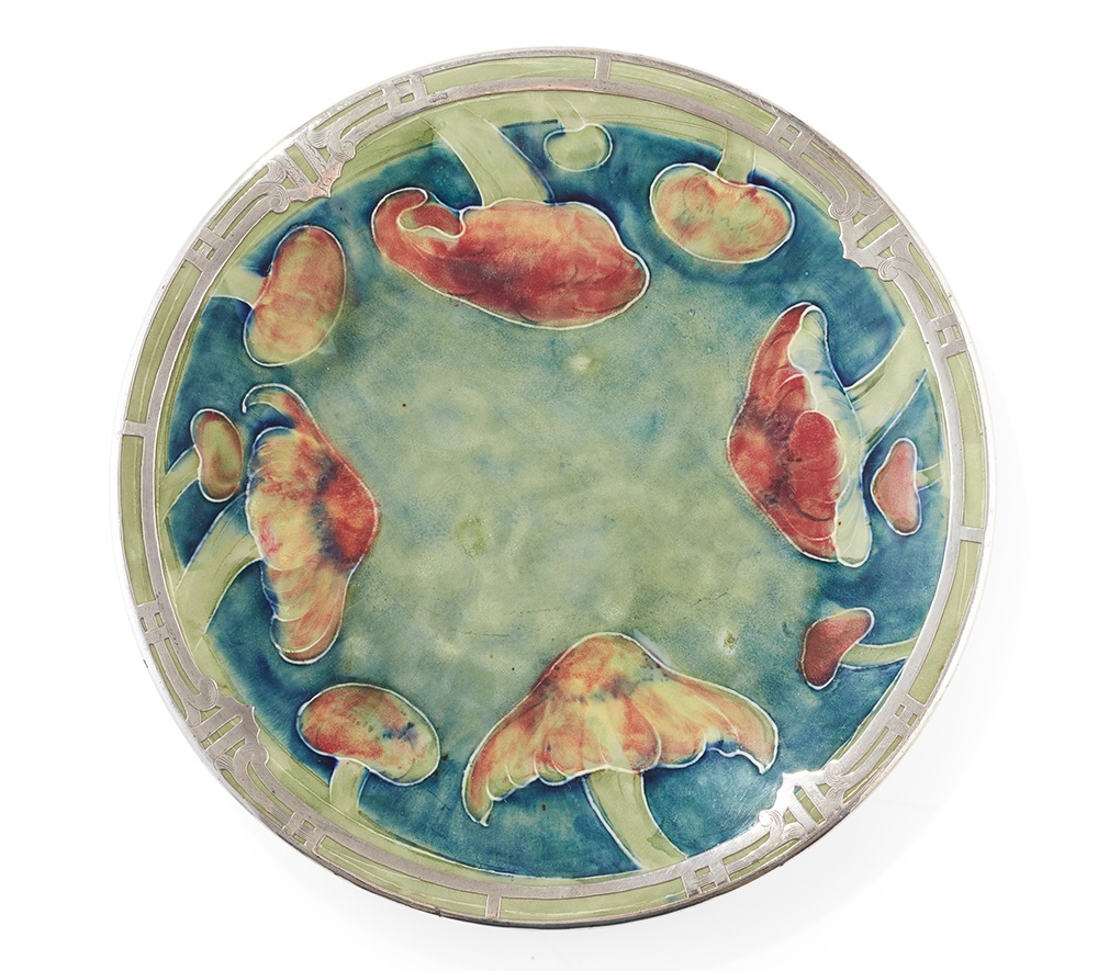 LOT 298 | WILLIAM MOORCROFT (1872-1945) FOR SHREVES & CO., SAN FRANCISCO | ‘CLAREMONT’ PATTERN PLATE, CIRCA 1905 glazed earthenware, overlaid with while metal openwork rim, painted W. MOORCROFT/ SHREVES & COMPANY/ SAN FRANCISCO, printed registration number 420081 | 23.5cm diameter | £1,500 - £2,000 + fees
